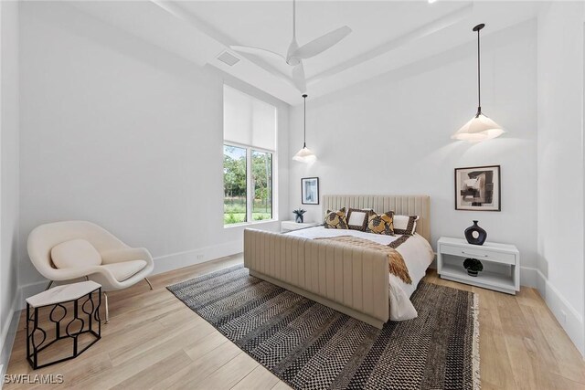 bedroom featuring visible vents, a towering ceiling, ceiling fan, light wood-type flooring, and baseboards