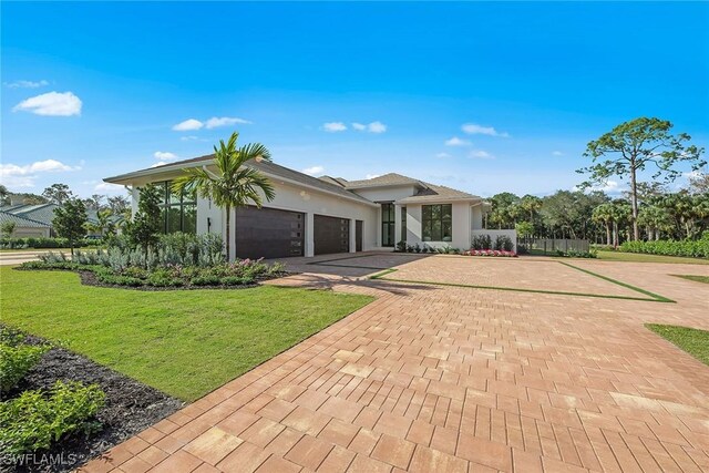 view of front of house featuring an attached garage, fence, decorative driveway, a front lawn, and stucco siding