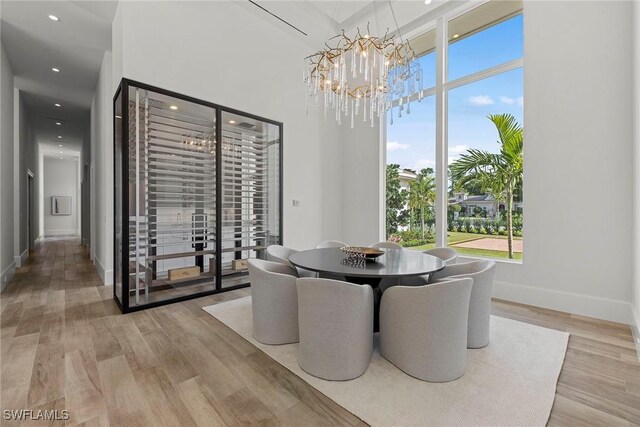 dining area with a towering ceiling, an inviting chandelier, baseboards, and light wood-style floors