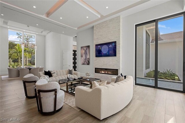 living area with a stone fireplace, recessed lighting, a high ceiling, light wood-type flooring, and beam ceiling