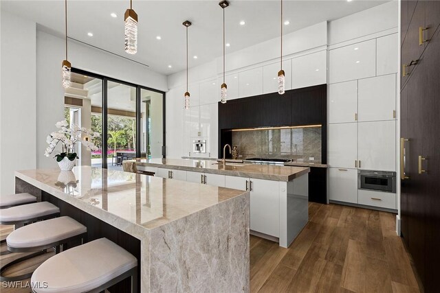 kitchen featuring a kitchen island with sink, white cabinets, light stone countertops, modern cabinets, and pendant lighting