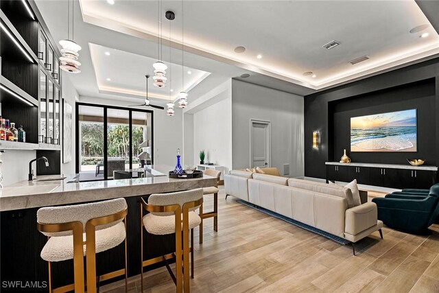 kitchen with open floor plan, a tray ceiling, light countertops, light wood-type flooring, and pendant lighting