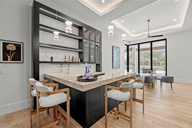 bar featuring a tray ceiling, pendant lighting, indoor wet bar, light wood-style flooring, and baseboards