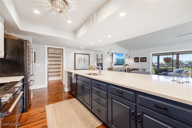 kitchen with light stone countertops, stainless steel appliances, blue cabinets, sink, and hardwood / wood-style floors