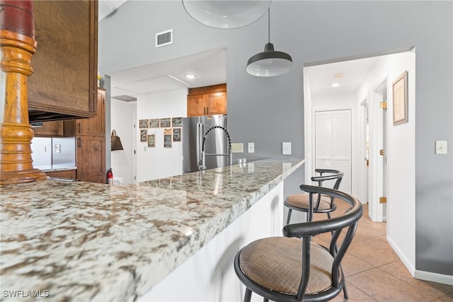 kitchen featuring kitchen peninsula, a breakfast bar area, light tile patterned floors, stainless steel refrigerator, and light stone counters