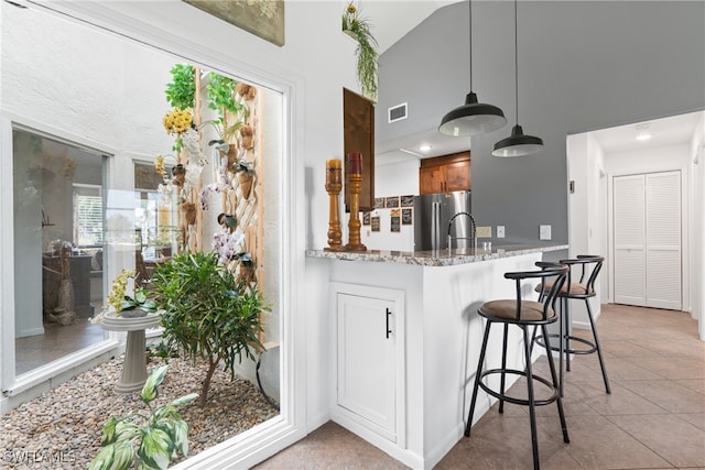 kitchen featuring a kitchen breakfast bar, pendant lighting, light tile patterned floors, light stone counters, and stainless steel refrigerator