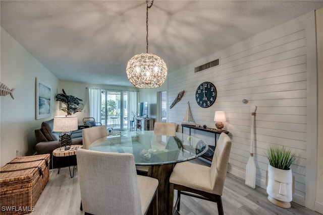 dining room with light wood-type flooring, a textured ceiling, wooden walls, and an inviting chandelier