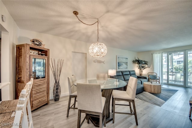 dining space featuring light wood-type flooring, a textured ceiling, and an inviting chandelier