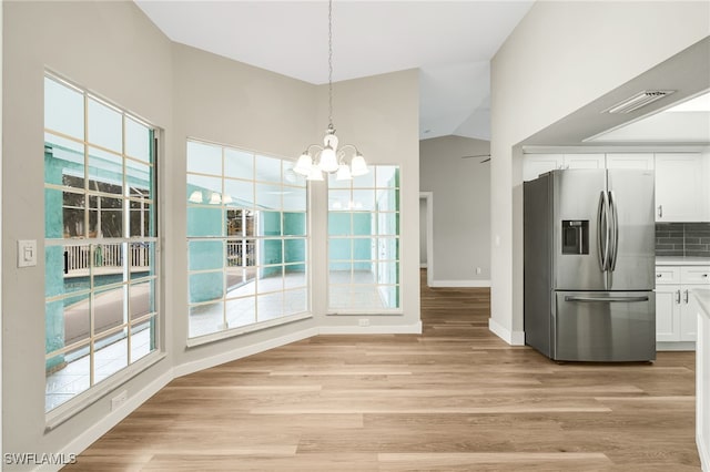 unfurnished dining area with light wood-type flooring, a notable chandelier, lofted ceiling, and plenty of natural light