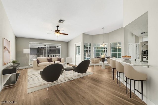 living room with hardwood / wood-style flooring, vaulted ceiling, and ceiling fan with notable chandelier