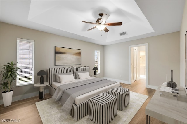 bedroom featuring multiple windows, light wood-type flooring, and a raised ceiling