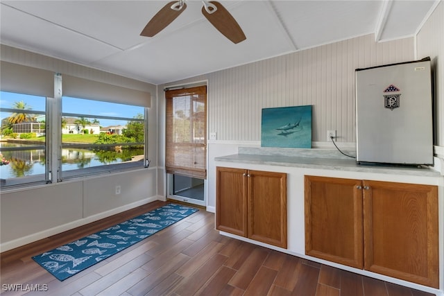 kitchen featuring stainless steel fridge, a water view, dark wood-type flooring, wood walls, and ceiling fan