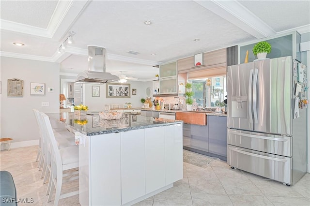 kitchen with island exhaust hood, appliances with stainless steel finishes, dark stone countertops, and white cabinetry