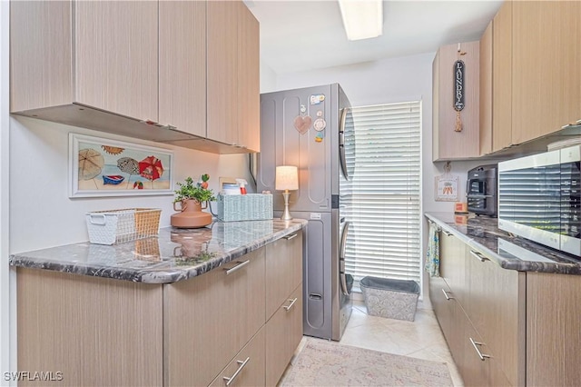 kitchen with light brown cabinetry, light tile patterned floors, appliances with stainless steel finishes, and dark stone countertops