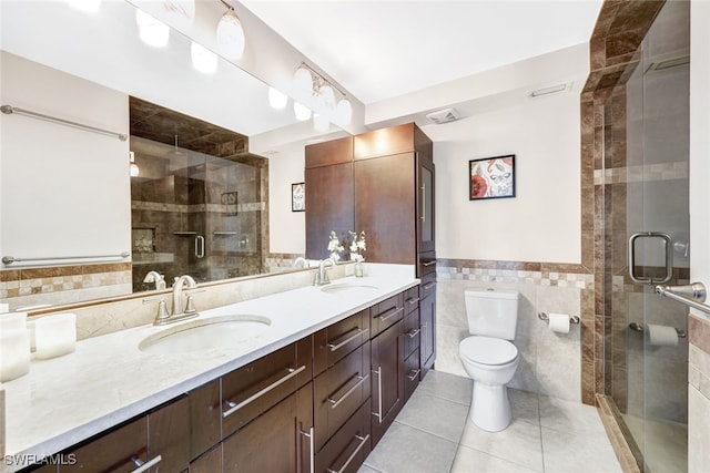 bathroom featuring toilet, vanity, tile walls, tile patterned floors, and a shower with shower door