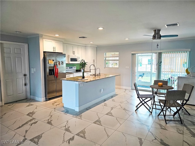 kitchen with ceiling fan, white appliances, decorative light fixtures, a kitchen island with sink, and white cabinetry