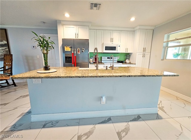 kitchen with light stone counters, white appliances, a kitchen island with sink, white cabinetry, and crown molding