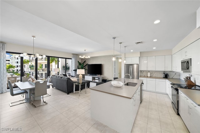 kitchen with backsplash, a kitchen island with sink, an inviting chandelier, white cabinets, and appliances with stainless steel finishes