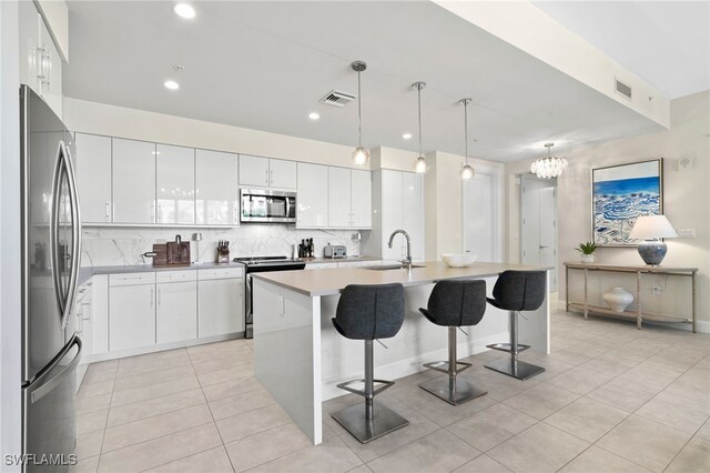 kitchen with decorative light fixtures, a kitchen island with sink, a breakfast bar, white cabinets, and appliances with stainless steel finishes