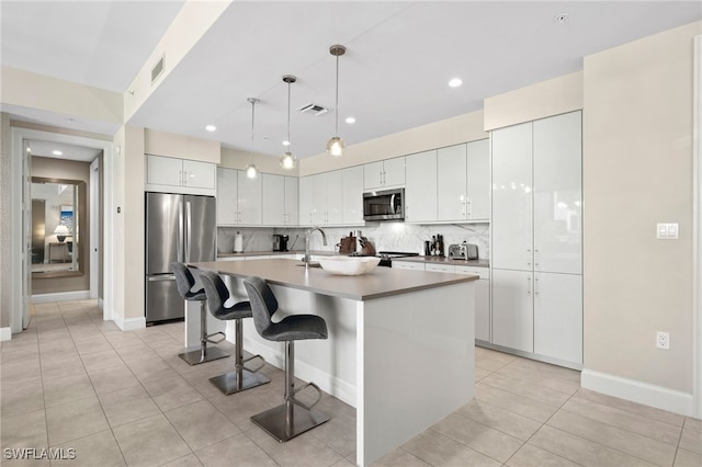 kitchen with stainless steel appliances, an island with sink, pendant lighting, decorative backsplash, and white cabinets