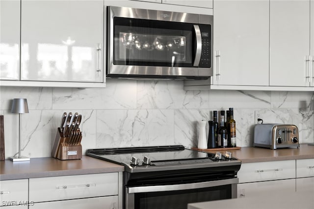 kitchen with backsplash, white cabinetry, and stainless steel appliances