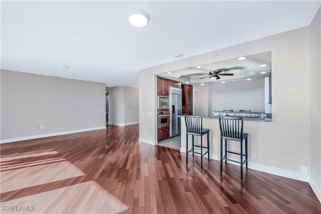 kitchen with kitchen peninsula, stainless steel fridge, a kitchen breakfast bar, a raised ceiling, and wood-type flooring