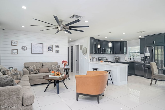 tiled living room with sink, wooden walls, and ceiling fan