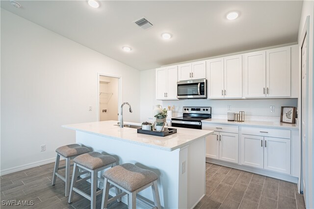 kitchen featuring stainless steel appliances, white cabinets, a kitchen island with sink, and sink