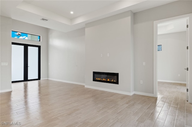 unfurnished living room with light wood finished floors, a glass covered fireplace, baseboards, a tray ceiling, and visible vents