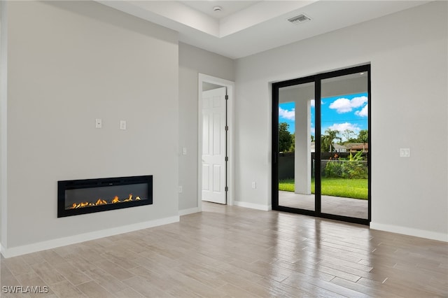 unfurnished living room featuring a glass covered fireplace, baseboards, light wood-type flooring, and visible vents
