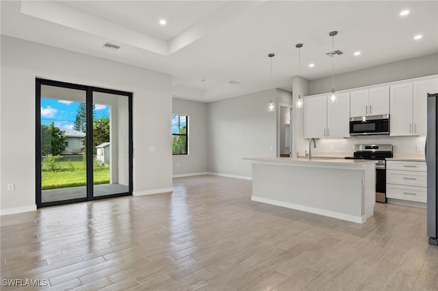 kitchen with appliances with stainless steel finishes, white cabinetry, decorative light fixtures, and an island with sink