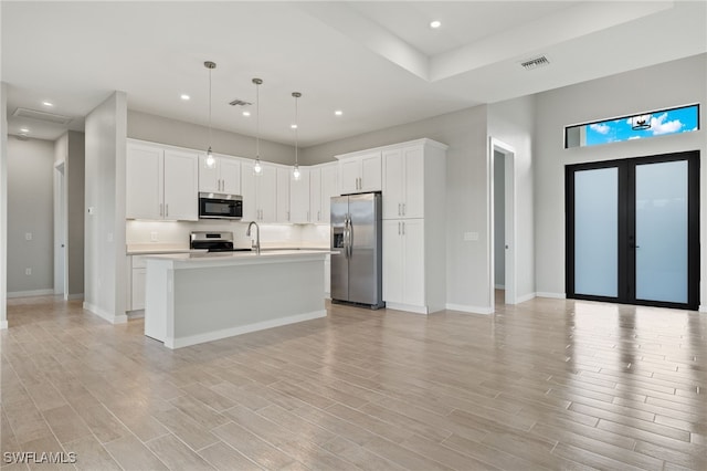 kitchen with pendant lighting, light hardwood / wood-style flooring, stainless steel appliances, and white cabinets