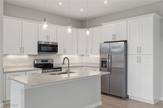 kitchen featuring hanging light fixtures, stainless steel appliances, a center island with sink, sink, and white cabinetry