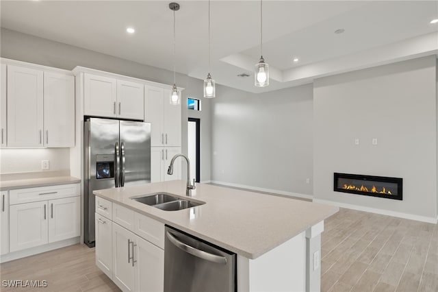 kitchen featuring white cabinets, a sink, light wood finished floors, appliances with stainless steel finishes, and hanging light fixtures