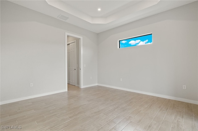 spare room with a tray ceiling and light wood-type flooring