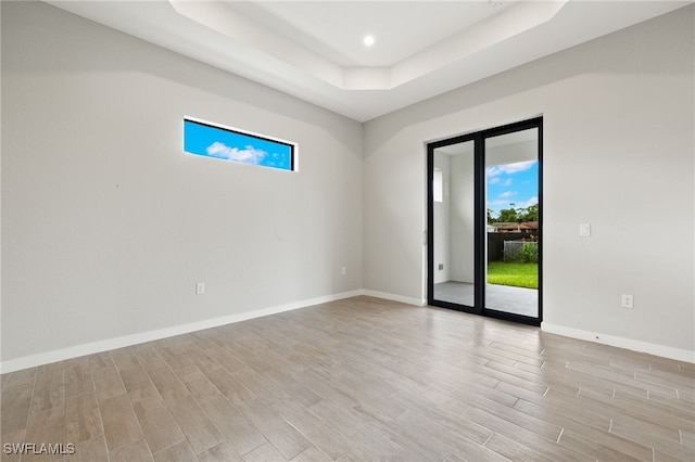 unfurnished room featuring a raised ceiling, plenty of natural light, baseboards, and light wood finished floors