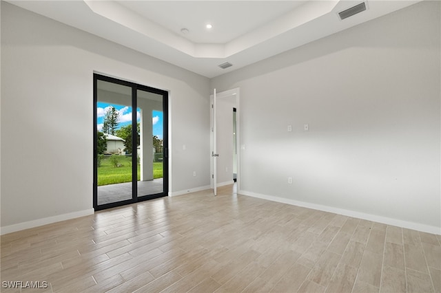 unfurnished room featuring a tray ceiling and light hardwood / wood-style floors