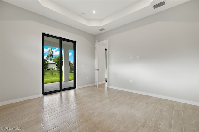 unfurnished room featuring visible vents, light wood finished floors, baseboards, and a tray ceiling