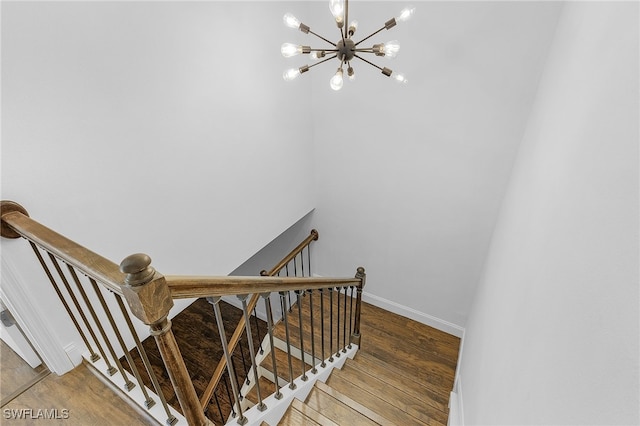 stairway with wood-type flooring and an inviting chandelier