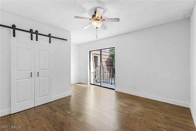 unfurnished room with a textured ceiling, ceiling fan, dark wood-type flooring, and a barn door