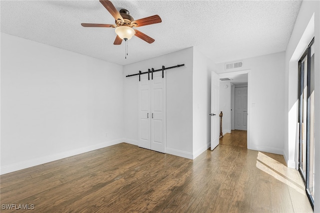 unfurnished room featuring a barn door, a textured ceiling, hardwood / wood-style floors, and ceiling fan