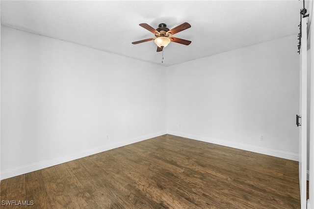 empty room featuring ceiling fan, a textured ceiling, a barn door, and dark wood-type flooring