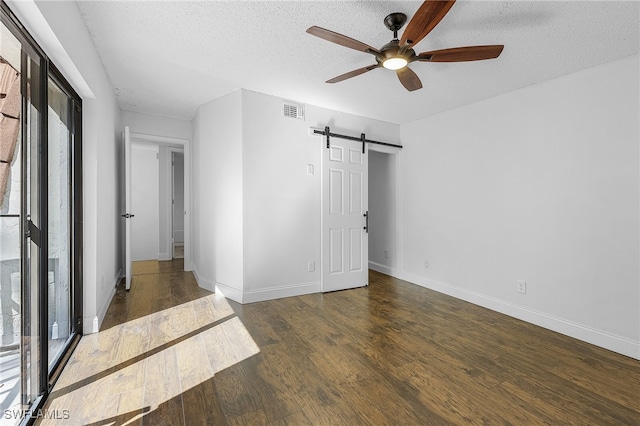 unfurnished bedroom featuring a barn door, a textured ceiling, dark hardwood / wood-style flooring, and ceiling fan