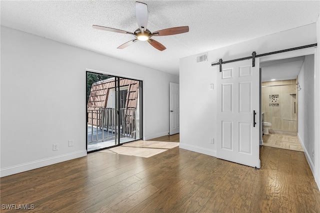 empty room featuring ceiling fan, a textured ceiling, hardwood / wood-style floors, and a barn door