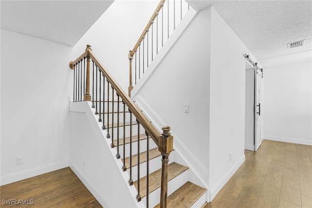 stairs with a barn door, a textured ceiling, and hardwood / wood-style flooring