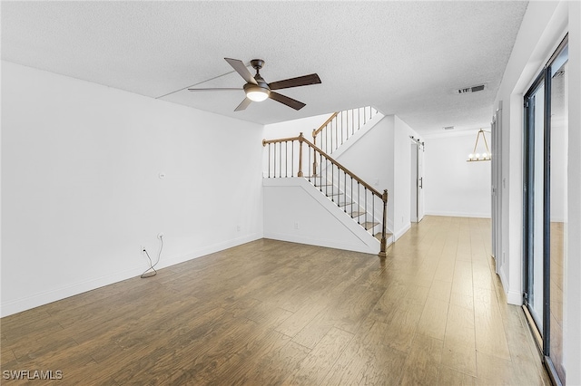 unfurnished living room with a barn door, wood-type flooring, a textured ceiling, and ceiling fan