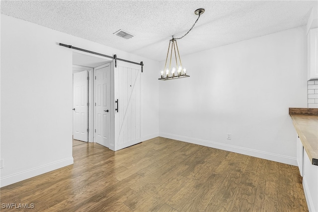 unfurnished dining area featuring a barn door, a textured ceiling, and hardwood / wood-style floors