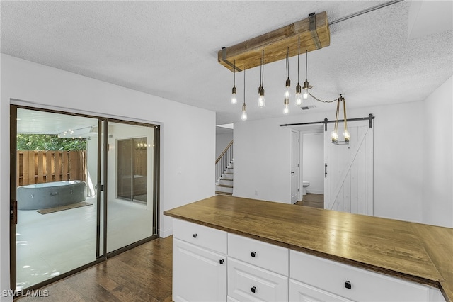 kitchen with a textured ceiling, decorative light fixtures, white cabinetry, dark hardwood / wood-style floors, and a barn door