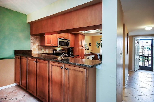 kitchen with light tile patterned flooring, dark stone countertops, appliances with stainless steel finishes, kitchen peninsula, and decorative backsplash