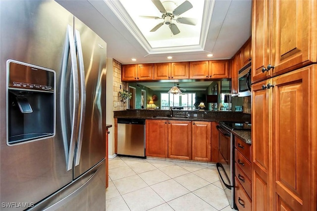 kitchen with a sink, stainless steel appliances, brown cabinetry, a tray ceiling, and a ceiling fan